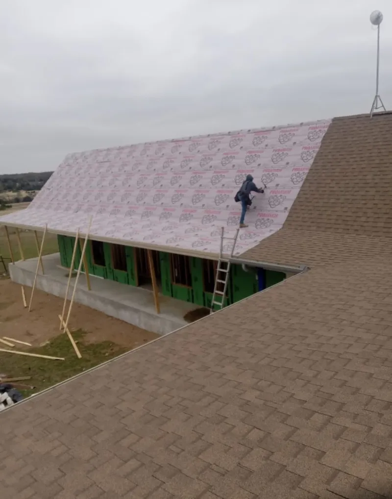 Worker preparing underlayment for a metal roof installation in Kirby